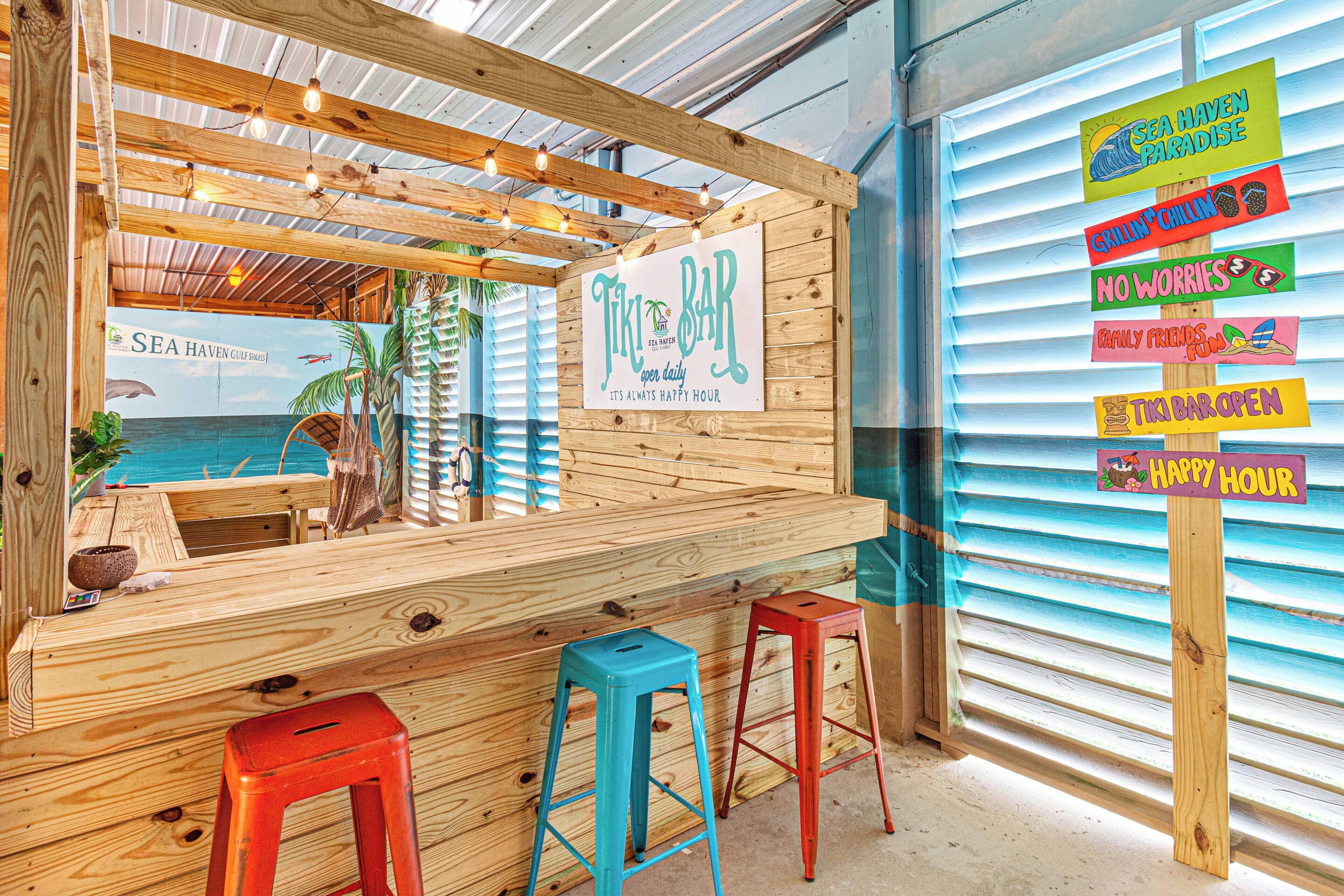 A wooden bar area with a sign reading 'Tiki Bar' and various colorful signs advertising services like 'Grillin' Chillin'' and 'No Worries'.