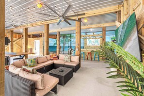A spacious indoor area with a large sectional sofa, a ceiling fan, and a view of the ocean through large windows. - SeaHaven @ Laguna Key- 6BR "Almost Beachfront" Home, Pool, Tiki Bar, Game Garage (Gulf Shores)