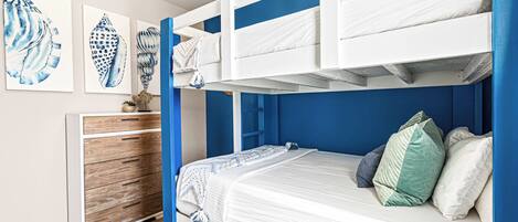 A bunk bed room with a wooden dresser, a blue accent wall, and artwork on the wall.