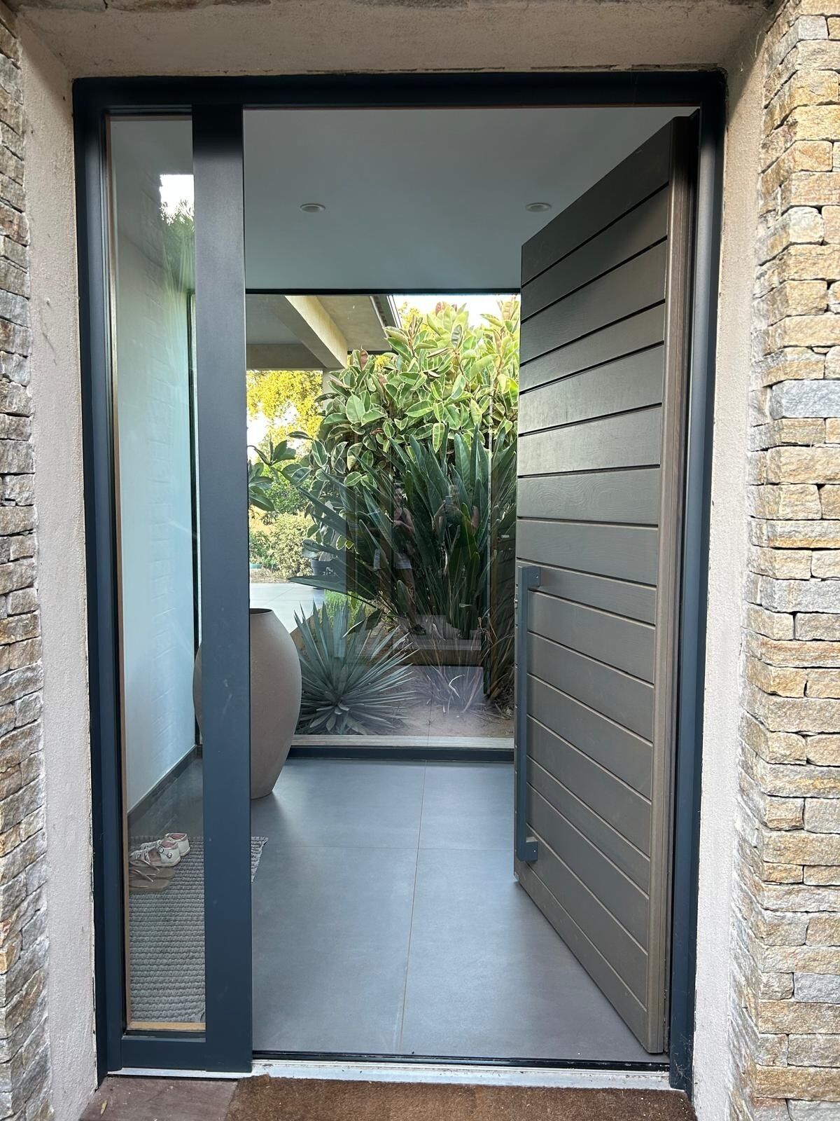 A modern entrance with a sliding glass door leading to a patio area with plants and a large decorative stone.