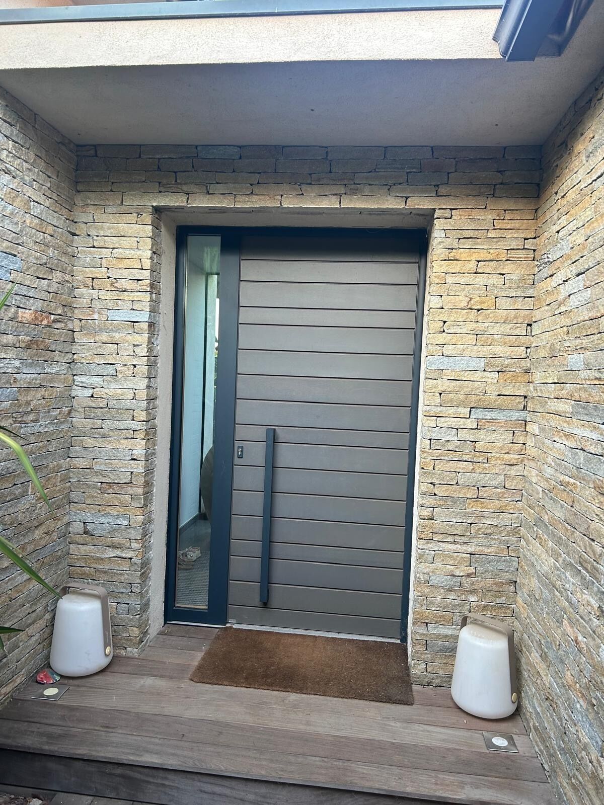 Une entrée moderne avec une façade en pierre, une porte coulissante et un petit espace de porche agrémenté de deux jardinières blanches.