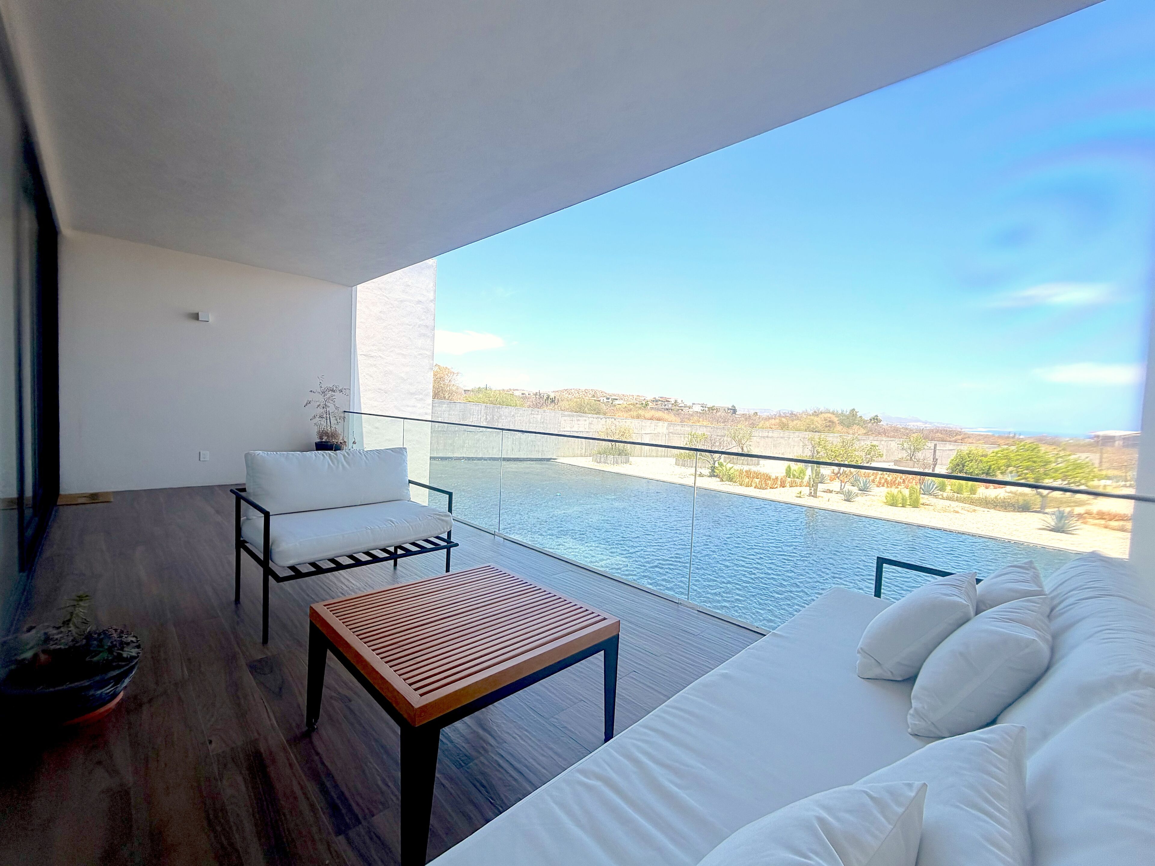 A modern balcony with a white sofa, a wooden table, and a chair.