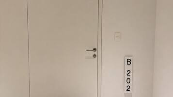 A room with a white door, a doormat with 'home sweet home' text, and a wall-mounted sign with 'B202'.