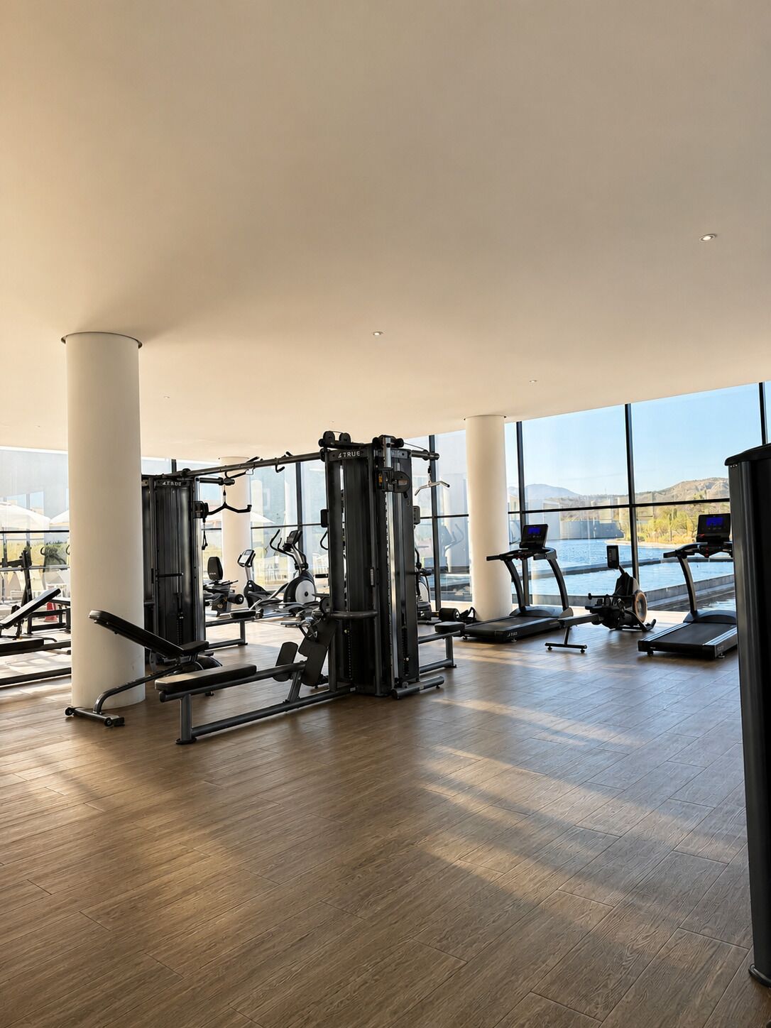 A spacious gym with various exercise equipment, large windows, and a high ceiling.