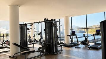 A spacious gym with various exercise equipment, large windows, and a high ceiling.