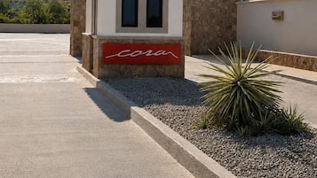 Un edificio pequeño con techo de tejas, un letrero rojo con la palabra 'coral' y un jardín con una planta de yuca.