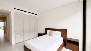 Un dormitorio moderno con una cama grande, cabecera de madera, ropa de cama blanca y un armario con puertas correderas.