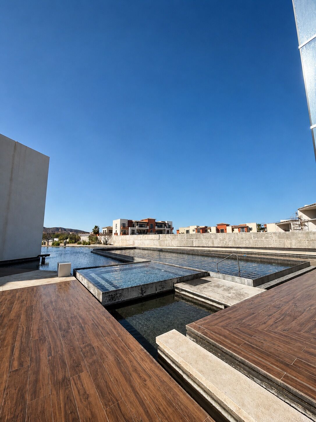Une piscine sur le toit, divisée en plusieurs zones, entourée d’une terrasse en béton et avec des bâtiments en arrière-plan.