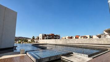 A rooftop swimming pool with multiple sections, surrounded by a concrete deck and buildings in the background.