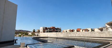 Une piscine sur le toit, divisée en plusieurs zones, entourée d’une terrasse en béton et avec des bâtiments en arrière-plan.
