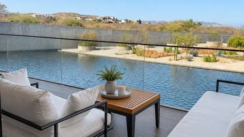 Un balcón con vista a un cuerpo de agua, una zona de estar con mesa y una barandilla.