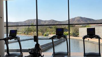 Un gimnàs amb cintes de córrer i una màquina d'a rem, grans finestres i vista a muntanyes i una piscina.