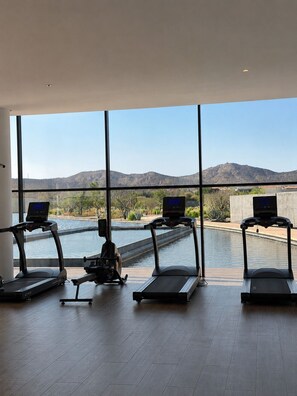 A gym with treadmills and a rowing machine, large windows, and a view of mountains and a pool. - 3Bdrm Luxury Condo I Pool &Jacuzzi I GYM (San José del Cabo)