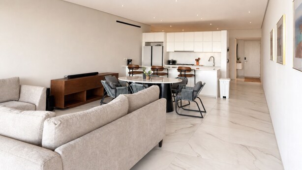 Una sala de estar moderna con un sofá, una zona de comedor con sillas y una cocina al fondo.