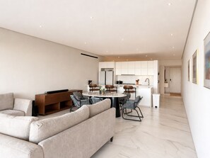A modern living room with a sofa, a dining area with chairs, and a kitchen in the background. - 3Bdrm Luxury Condo I Pool &Jacuzzi I GYM (San José del Cabo)