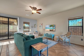A living room with a green sofa, a wooden coffee table, a blue side table, a chair, and a ceiling fan.