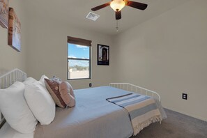 A bedroom with a bed, a window, a ceiling fan, and a wall-mounted picture. - Spacious Central Tucson Home • Garage & Dogs OK (Tucson)