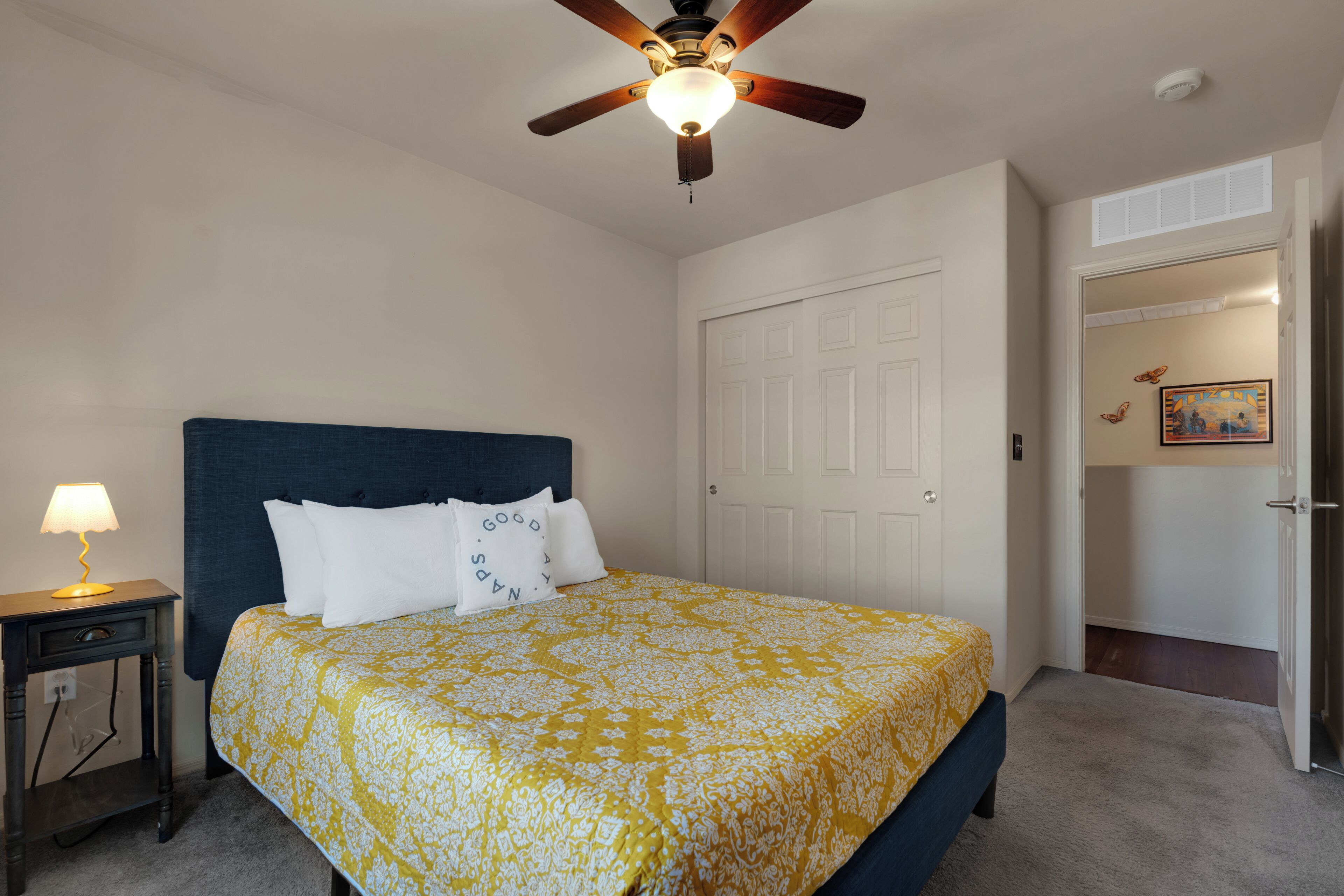 A bedroom with a bed, a nightstand, a ceiling fan, and a door.
