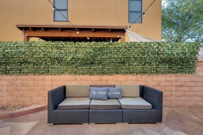 A wicker sofa with cushions against a brick wall, under a pergola with string lights.