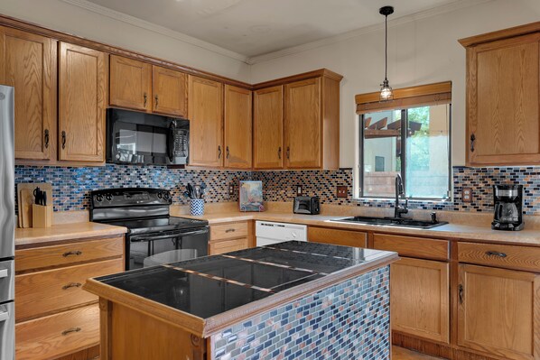 A kitchen with wooden cabinets, a black microwave, a stove, and a tiled backsplash. - Spacious Central Tucson Home • Garage & Dogs OK (Tucson)