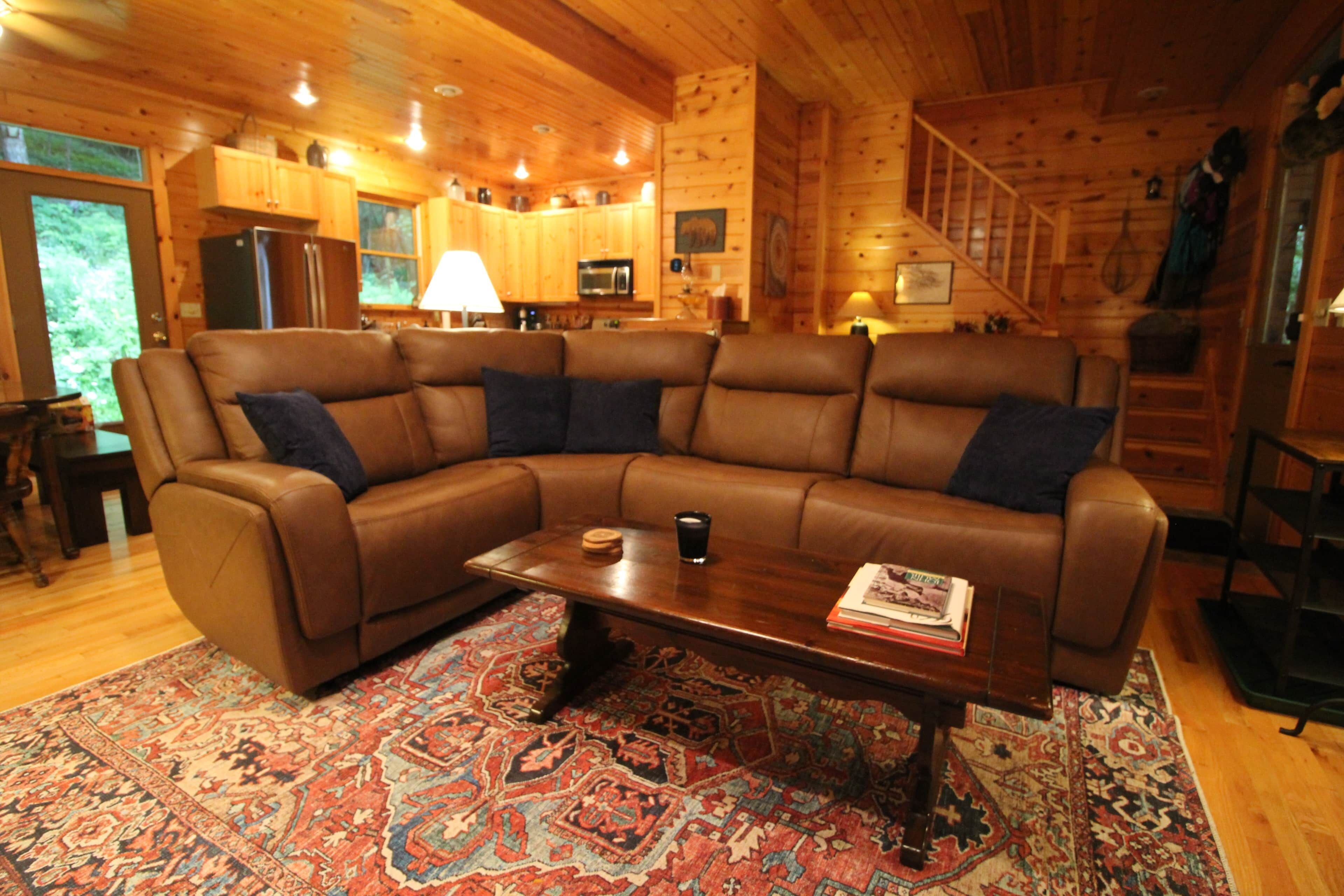 L’intérieur d’un chalet accueillant, avec un grand canapé d’angle marron, une table basse en bois et un tapis à motifs.