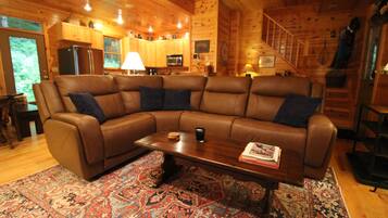 L’intérieur d’un chalet accueillant, avec un grand canapé d’angle marron, une table basse en bois et un tapis à motifs.