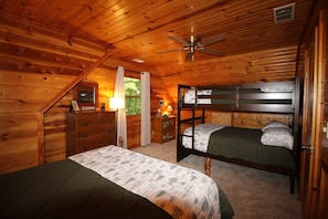 Une chambre dans une cabane en bois, avec un lit superposé, une commode, une lampe et un ventilateur de plafond.