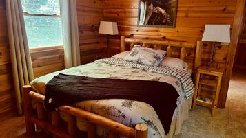 Une chambre à coucher dans une cabane en bois, avec un lit, deux lampes de chevet, une fenêtre et un tableau accroché au mur.