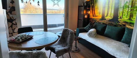 Una sala moderna con comedor, un ventanal con adornos de estrellas, un mural de bosque y un sofá acogedor.