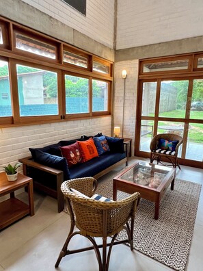 A living room with a sofa, wicker chairs, a coffee table, and large windows.
