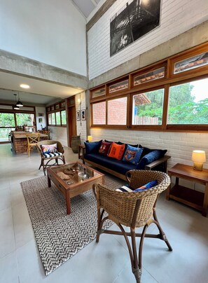 A spacious living area with a large sofa, wicker chairs, a coffee table, and a dining area with a bench and chairs.