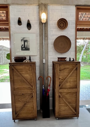 Two wooden cabinets with handles, a light fixture, a framed picture, and a decorative plate on a white brick wall. - #1 Rosário Marajó Residence - Água Boa - One Suite (Salvaterra)