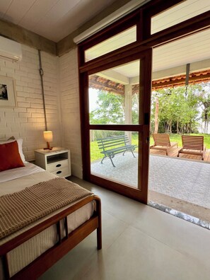 A bedroom with a bed, a nightstand, a lamp, and a view of an outdoor patio with a bench and chairs.