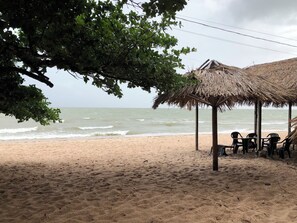 A beach with a thatched-roof structure, a sandy shore, and the ocean in the background.