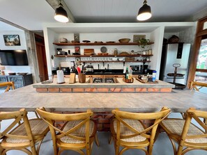 Une cuisine dotée d’un îlot central, de chaises en bois et de divers ustensiles de cuisine rangés sur des étagères.
