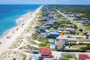 A coastal residential area with beachfront properties, a swimming pool, and a beach with umbrellas. - 8 Bed Oceanfront w Pool/Spa, Private Beach Access! (Nags Head)