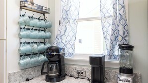 Una cocina con cafetera, licuadora y un frutero lleno de tazas.