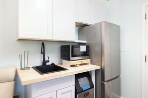 A compact kitchen with a built-in microwave, a stainless steel refrigerator, and a small sink. - 8 Bed Oceanfront w Pool/Spa, Private Beach Access! (Nags Head)