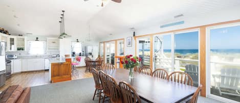 A spacious kitchen with modern appliances, a dining area with a large table and chairs, and a view of the ocean through large windows.