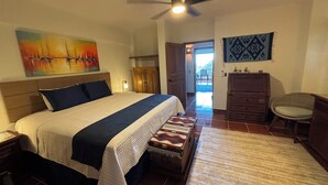 Ein Schlafzimmer mit einem Bett, einem Deckenventilator, einem Gemälde, einer Kommode und einem Stuhl.