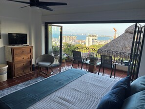 Een balkon met uitzicht op de stad en de zee, een bank, een televisie en een houten dressoir.