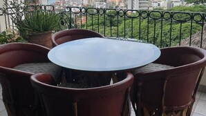 Ein runder Tisch mit sechs Stühlen auf einem Balkon mit Metallgeländer, Blick auf Stadt und Meer.