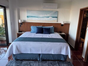 A hotel room with a bed, a painting of waves, a wooden headboard, and a nightstand with a lamp. - 2 bedroom condo with panoramic views of Romantic Zone, bay and mountains (Puerto Vallarta)