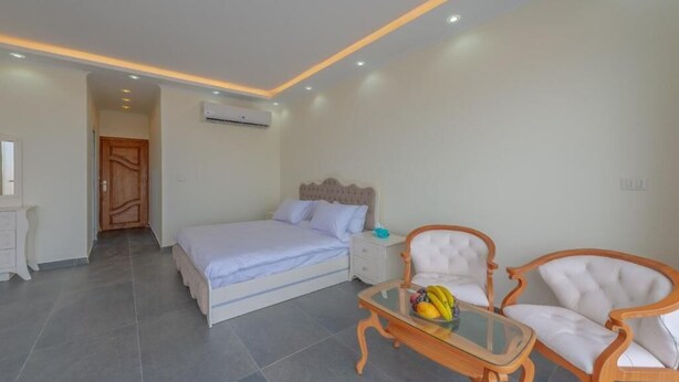 A bedroom with a bed, bedside table, two chairs, and a small table with fruit.