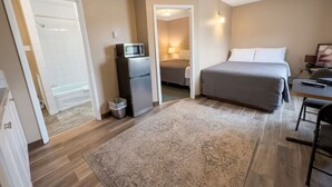 Un dormitorio con cama, escritorio, silla, microondas y basurero.