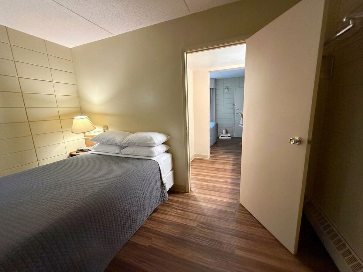 A hotel room with a bed, bedside lamp, and a view into the bathroom.