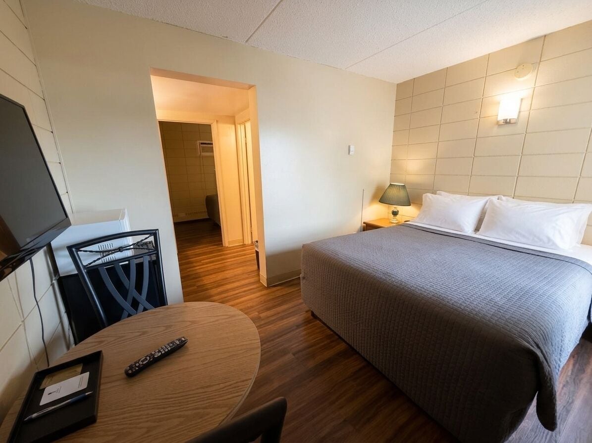 A hotel room with a bed, a desk with a chair, a TV, and a lamp.