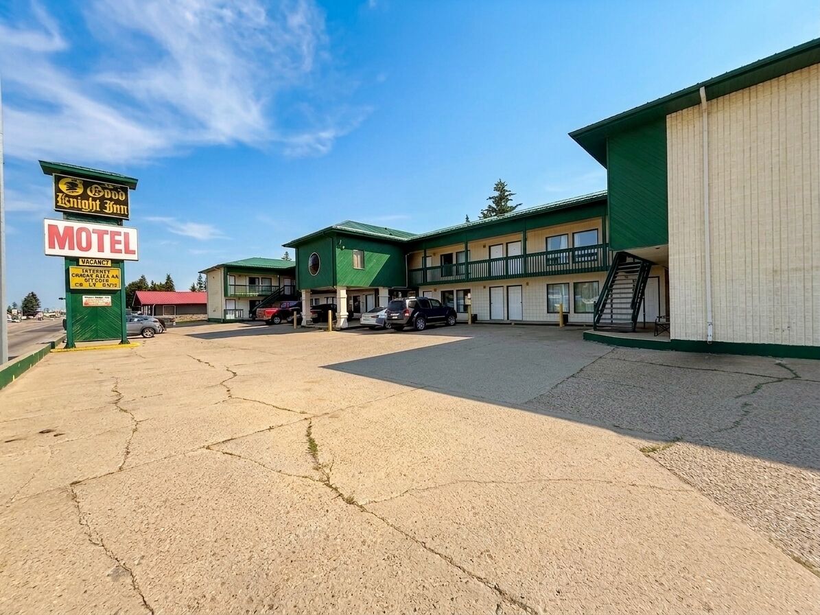A motel with a green exterior, multiple parking spaces, and a sign indicating vacancy.