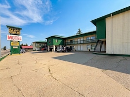 Un motel con fachada verde, varios espacios de estacionamiento y un letrero que indica disponibilidad.