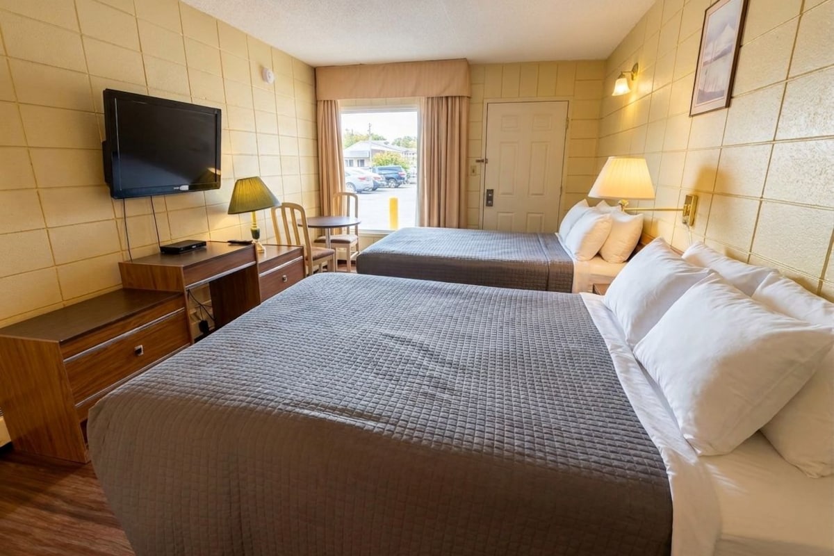 A hotel room with two beds, a television, a desk with a lamp, and a view of the outside.